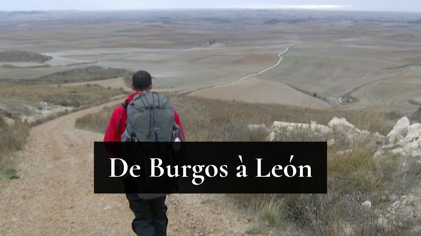 Un pèlerin sac au dos descend une piste caillouteuse face à l'immensité de la Meseta, entre Burgos et León