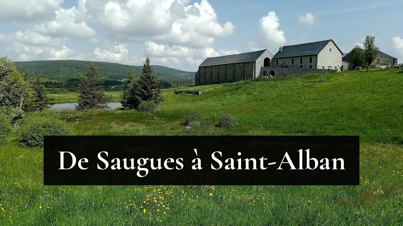 Les bâtiments de granit du domaine du Sauvage au-dessus d'un étang et de prés fleuris, sur le plateau de la Margeride