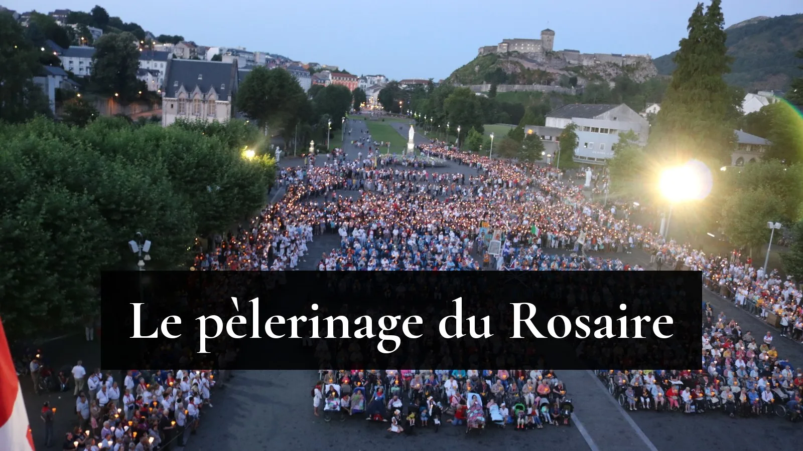 Procession aux flambeaux sur l'esplanade du Rosaire à Lourdes, les pèlerins malades en fauteuil au premier rang, le château fort au fond